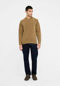 Maglione marrone lavorato a maglia con scollo rotondo, polsini e orlo a costine, abbinato a jeans blu scuro e scarpe in suede marroni.