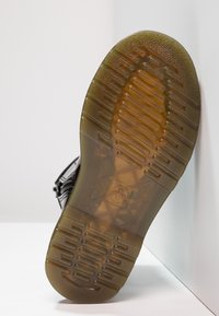 Suela de zapato de goma negra con patrones de agarre texturizados y secciones transparentes. Marca notable en el centro. Diseño limpio y minimalista.