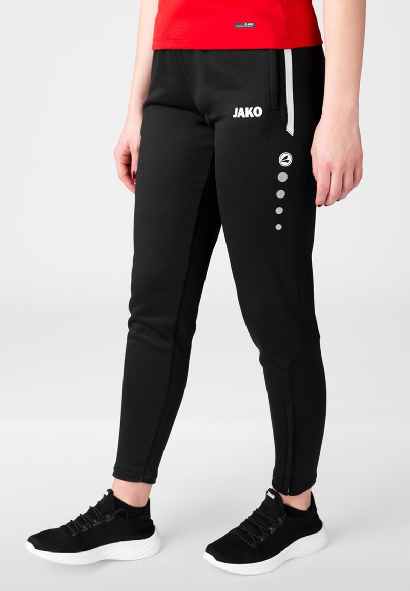 Zwarte sportbroek met een strak ontwerp, zij witte strepen, logo en decoratieve grijze cirkels. Gecombineerd met zwarte schoenen met een witte zool.