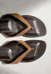 Tongs à brides en daim marron avec semelles rembourrées marron foncé, présentant un design à bout carré sur une surface gris clair.