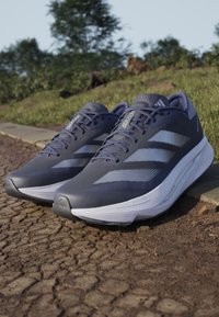 Modré bežecké topánky s textúrovaným sieťovým zvrškom, bielou strednou podošvou a výrazným dizajnom troch pruhov. Zaoblený prst a ľahká konštrukcia.