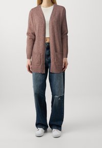 Sweter kardigan w jasnym mauve z prążkowanymi mankietami i dołem, z dwoma przednimi kieszeniami. Noszony na białym topie na krótko, w połączeniu z jeansami z przetarciami.