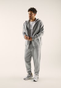 Gray sporty tracksuit made of soft fabric, featuring a zip-up hoodie and tapered pants, paired with silver and yellow athletic shoes.