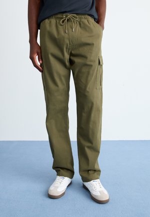 Olive green cargo pants with an elastic waistband and drawstring. Features side pockets and a relaxed fit. Worn with white sneakers.