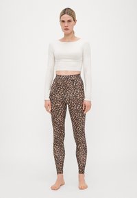 Un crop top blanc à manches longues associé à des leggings moulants au motif léopard noir et brun. Les jambes sont nues.
