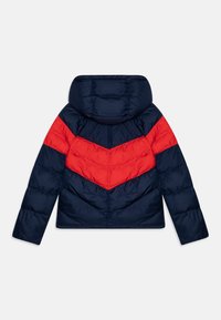 Puffatakki, jossa on laivastonsininen vartalo ja punaiset viivamallit hartioilla. Varustettu hupulla ja tikkikuvioinnilla.