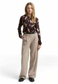 Top met lange mouwen met een meerkleurig abstract patroon, gecombineerd met beige, hooggetailleerde broek en zwarte plateauzolen, met een ontspannen pasvorm.