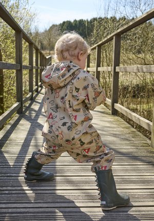 Beiger Regenanzug mit bunten Mustern, ausgestattet mit Kapuze und elastischen Bündchen, kombiniert mit dunkelgrünen Gummistiefeln mit Noppenakzenten.