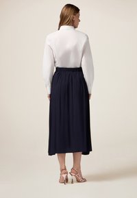 Blouse blanche avec col, manches ballon, et jupe maxi marine à taille élastique, associée à des talons roses à lanières.