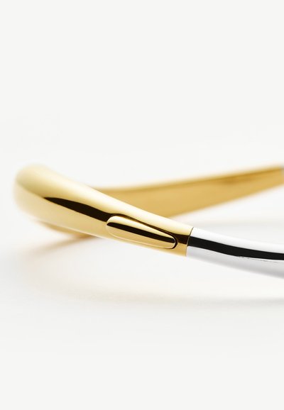 Κοντινό πλάνο ενός κομψού, χρυσού φορετού περιλαίμιου με ομαλή, καμπυλωτή σχεδίαση και ένα μικρό κουμπί στο πλάι.