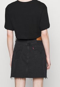 Czarny krótki t-shirt połączony z czarną dżinsową spódnicą z postrzępionym dołem i dwiema tylnymi kieszeniami z kontrastowym ściegem.