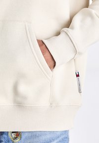 Kaki sweatshirt med en framficka, ribbade ärmslut och nederkant; har en liten logotagg på sidan och en mjuk textur.
