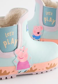 Bottes en caoutchouc bleu clair avec doublure beige. Présentent un texte "Let's Play", des accents roses et un autocollant de personnage de dessin animé sur le côté.