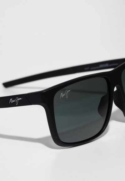 Zwarte zonnebril met grijze lenzen, matte afwerking, vierkant frame ontwerp, met zilveren "Maui Jim" merknaam op de armen.