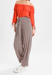 Czerwona bluzka bez ramiączek z falbaną i rękawami o długości trzy czwarte, w zestawieniu z wzorzystymi spodniami o szerokich nogawkach i białymi sneakersami z grafiką zwierząt.