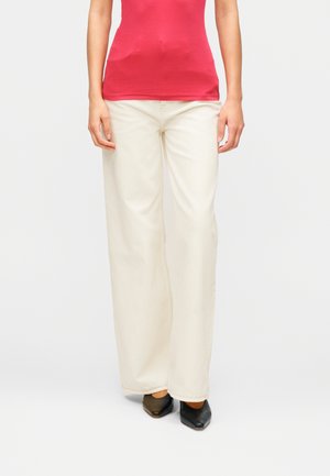 Lys beige, vide bukser laget av bomull, med sømdetaljer og rett snitt, kombinert med svarte spisse sko.