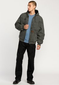Gray hooded jacket with a textured surface, front zipper, and elastic cuffs, paired with a blue shirt and black cargo pants.