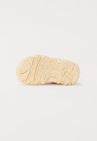 Semelle de chaussure de sport présentant une surface en caoutchouc texturé de couleur crème, avec un motif complexe pour l'adhérence et la traction.