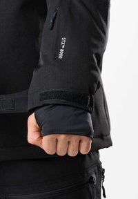 Schwarze, wasserdichte Jackenärmel mit einem Klettverschlussbund, der mit dem weißen "SIX™ 8000" Branding und einem strukturierten, mehrschichtigen Stoffdesign versehen ist.