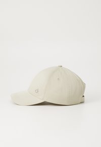 Cappellino da baseball beige in tessuto, con visiera curva, sei pannelli e un piccolo logo sul lato. Cinghia regolabile sul retro.