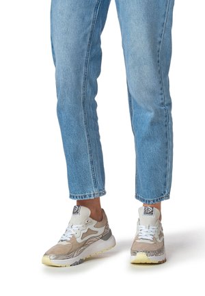 Sneakers with a light beige suede upper, white accents, and reflective silver details. Features laces, a cushioned sole, and a textured design.