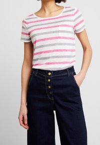 Camiseta de algodón con rayas horizontales rosa y gris, mangas cortas y un bolsillo en el pecho. Combinada con pantalones de mezclilla oscuros de cintura alta.