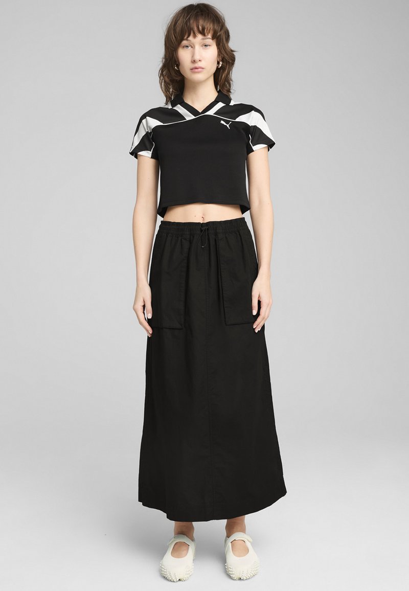 Juodas trumpas viršus su geometriniu baltu raštu, laisvi juodi sijonai su kišenėmis, ir balti neslidi batai su tekstūruotais akcentais.