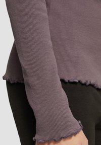 Paarse geribde lange mouwen top met een geribde zoom en manchetten, gemaakt van een zachte stof. Gecombineerd met zwarte onderkleding voor contrast.