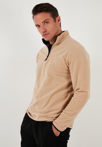 Beez fleecest pullover pooledega pooltõmbe kaeluses, must aksent kaelas, pikad varrukad, pehme tekstuur ja vrijas sobivus.