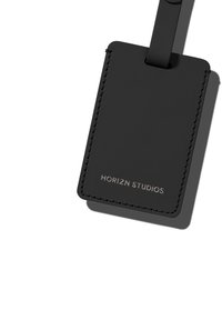Étiquette de bagage en cuir noir avec une texture lisse, des coins arrondis et des bords cousus. Présente un logo argenté "HORIZN STUDIOS".