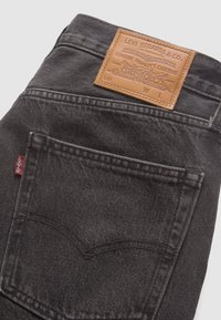 Mørkegrå denim jeans med et læderpatch med prægede bogstaver. Inkluderer en baglomme med syningsdetaljer og et rødt logo-label.