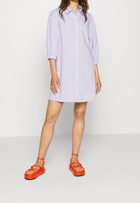 Světle fialové šaty na knoflíky s límečkem a tříčtvrtečními rukávy. V kombinaci s jasně oranžovými sandály na platformě s pásky.