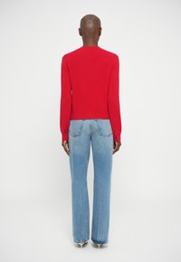 Červený pletený sveter s dlhými rukávmi, priliehavý v páse. Spárovaný s bledučko modrými nohavicami s vysokým pásom a širokými nohavicami. Minimalistický dizajn, žiadne viditeľné vzory.