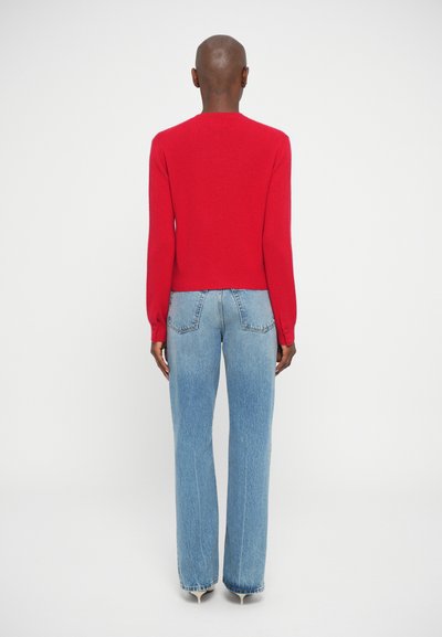 Pulover tricotat roșu cu mâneci lungi, ajustat la talie. Potrivit cu blugi evazați cu talie înaltă, de culoare albastru deschis. Design minimalist, fără modele vizibile.