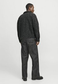 Veste texturée noire et grise avec un col, coupe ample et manches longues, assortie à un pantalon droit en denim foncé et des chaussures noires.