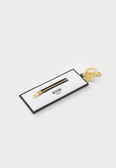 Breloză din piele neagră cu o etichetă albă, dotată cu un fermoar auriu și logo-ul Moschino Milano. Include accesorii aurii și un pandantiv circular.