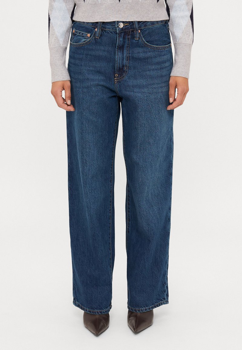 Široke jeans hlače v temno modri barvi, ki vključujejo klasičen dizajn s petimi žepi, zanke za pas in subtelno teksturirano zaključek.