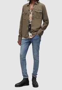 Olivgrön knäppskjorta över en blommig topp, matchad med ljusblå passande jeans och svarta ankelstövlar med minimal detaljer.