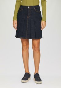 Denim rok met plooien, donkerblauwe kleur, oranje stiksels, vijf zakken en een knoopsluiting. Gecombineerd met zwarte sneakers.
