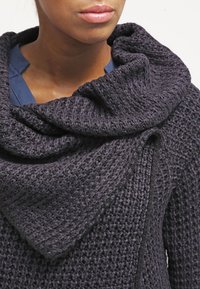 Chunky stickad tröja i mörkgrå, med en bred, draperad krage och strukturerat mönster. Mjuk material med en avslappnad passform.