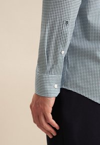 Camicia da uomo in tessuto azzurro chiaro con un motivo geometrico verde scuro. Presenta polsini con bottoni e una texture liscia con una vestibilità su misura.