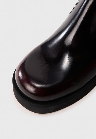 Λείο μπορντό δερμάτινο μπότες με στρογγυλεμένη μύτη, αντιθετική μαύρη ελαστική σόλα και εμφανείς ραφές κατά μήκος της άκρης της σόλας.