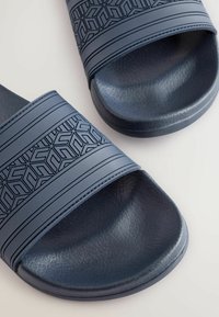 Le ciabatte di gomma blu presentano una superficie testurizzata con motivi geometrici e due larghe cinghie. La suola è leggermente sagomata per garantire comfort.