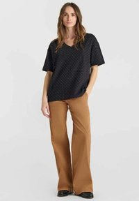 Top negro de cuello en V con patrón de puntos, combinado con pantalones acampanados color canela. El top tiene mangas cortas y un corte holgado, mientras que los pantalones son de largo hasta el suelo.