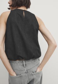 Zwarte mouwloze top met een keyhole-details aan de achterkant, gecombineerd met lichtgrijze high-waisted jeans met achterzakken en een gestructureerde afwerking.