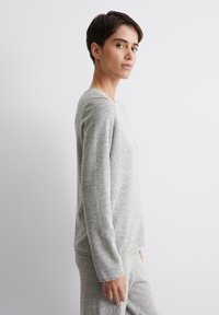 Szary sweter wykonany z miękkiego, teksturowanego materiału, z długimi rękawami i okrągłym dekoltem, przedstawiony z boku z pasującym dołem.