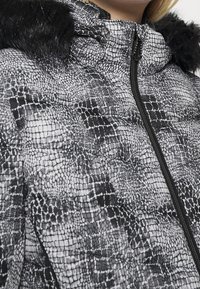 Kurtka puchowa w czarno-białym wzorze węża, z zamkiem błyskawicznym oraz teksturowym wykończeniem z futerkiem sztucznym na kapturze.