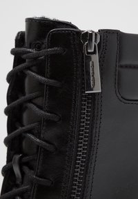 Boot in pelle nera con lacci e zip laterale. La zip presenta un tirante in argento lucido, e il boot ha una texture liscia e opaca.