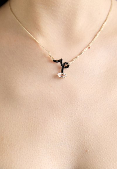 Collier en chaîne dorée avec un accent courbé noir et un pendentif en pierre précieuse ovale transparente. Texture lisse et design minimaliste.