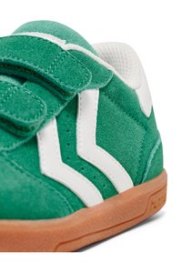 Baskets en daim vert avec accents blancs et une sangle à crochets, dotées d'une semelle en caoutchouc texturé et d'un design en zigzag sur les côtés.